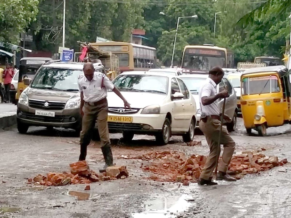 Policemen fill potholes with bricks in a rain lashed Chennai