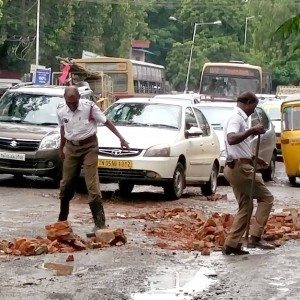 Policemen fill potholes with bricks in a rain lashed Chennai